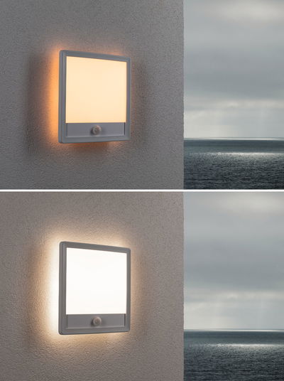 Quadratische graue Außenwandleuchte mit Bewegungsmelder und warmweißem Licht an Hauswand.