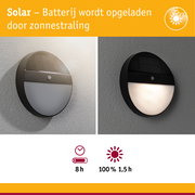 Ronde zwarte solar wandlamp met bewegingssensor aan grijze muur, energiezuinige buitenverlichting