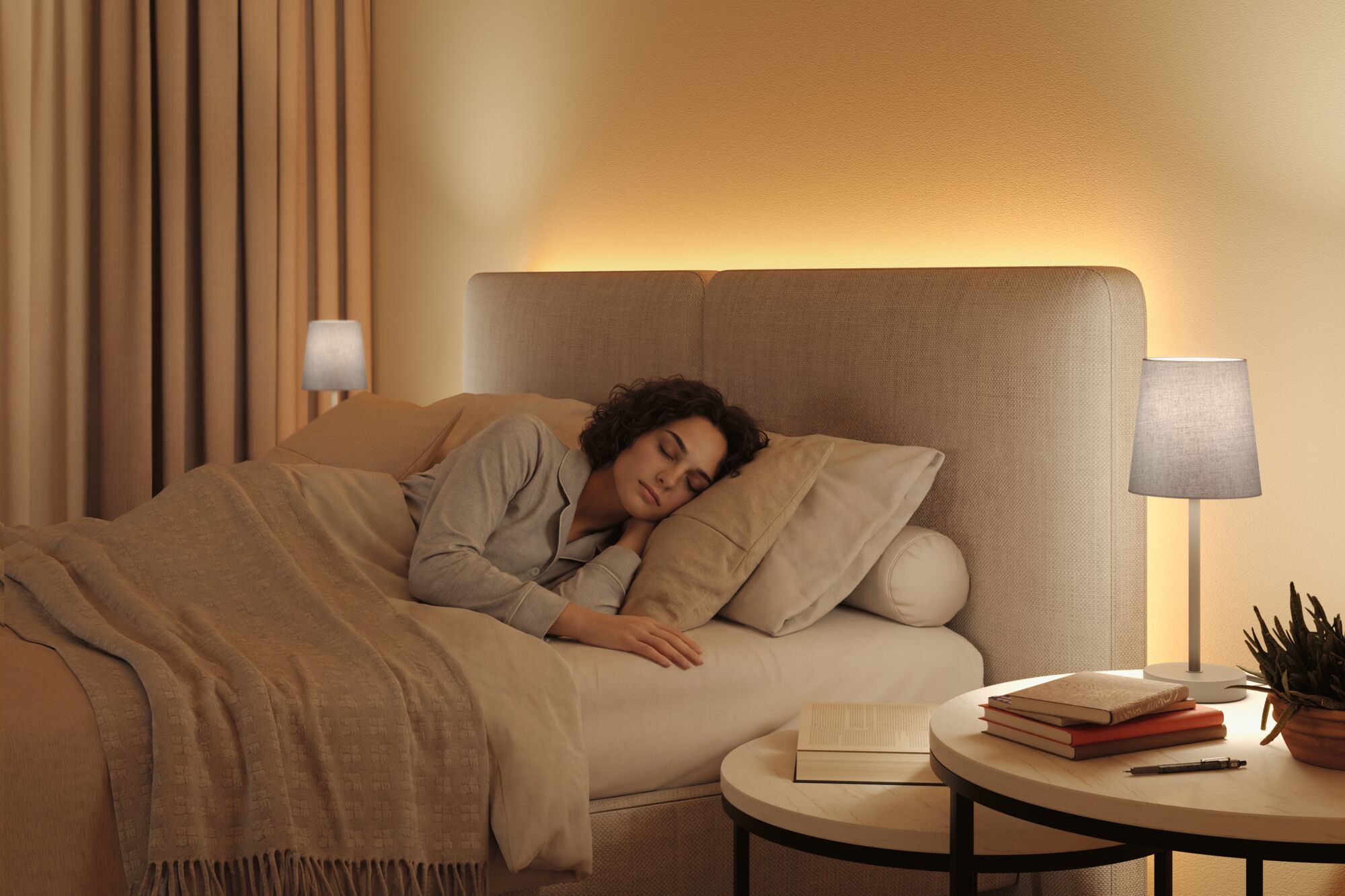 Bedroom with beige fabric bed, warm LED backlighting and grey table lamp on bedside table