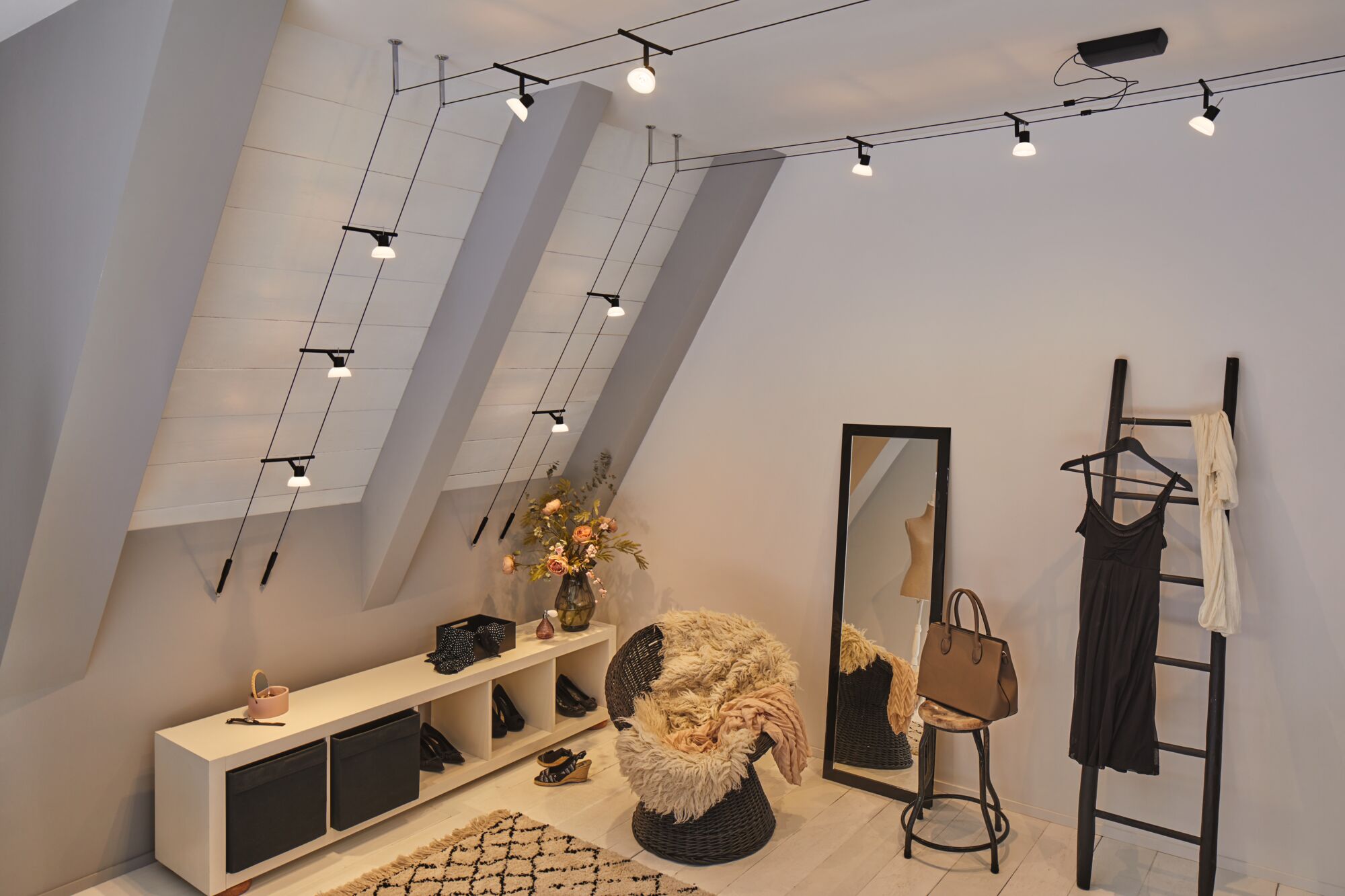 Schwarzes Kabel-Seilsystem mit weißen LED-Strahlern an schräger Decke in modernem Ankleidezimmer