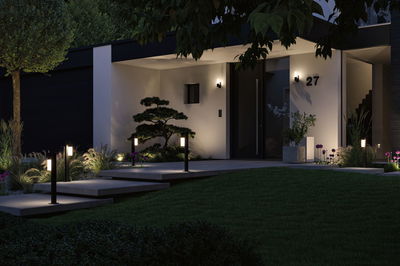 Éclairage extérieur moderne avec lampes LED noires sur poteaux et appliques murales devant maison et jardin.