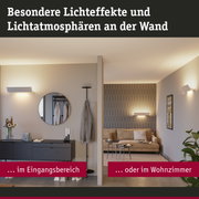 Moderne weiße Wandleuchten erzeugen warme Lichteffekte im Eingangsbereich und Wohnzimmer.