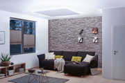 Moderne woonkamer met indirecte MaxLED plafondverlichting in daglichtwit en grijze stenen muur.