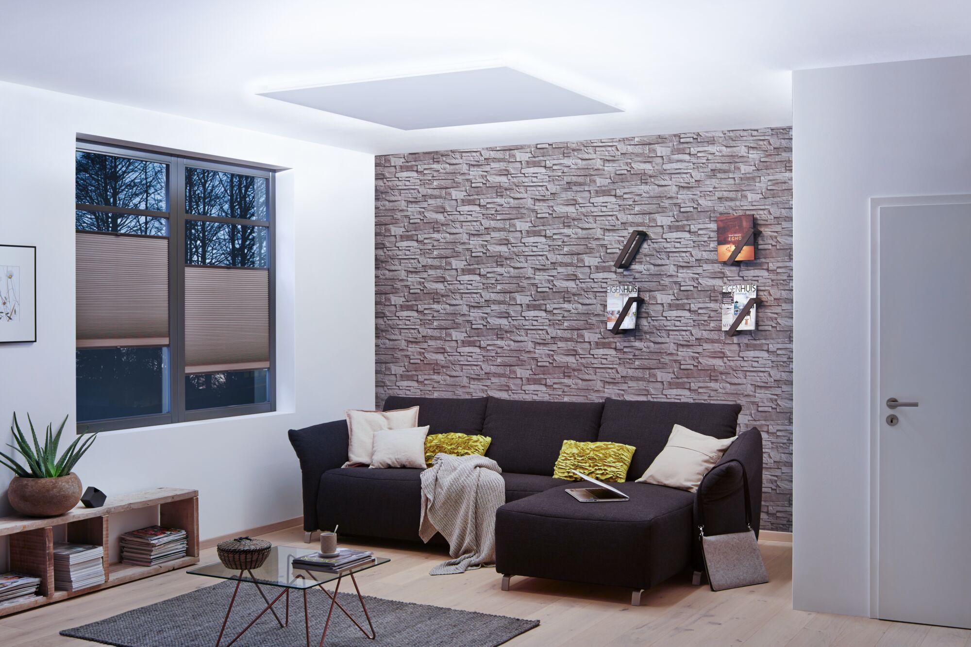 Moderne woonkamer met indirecte MaxLED plafondverlichting in daglichtwit en grijze stenen muur.