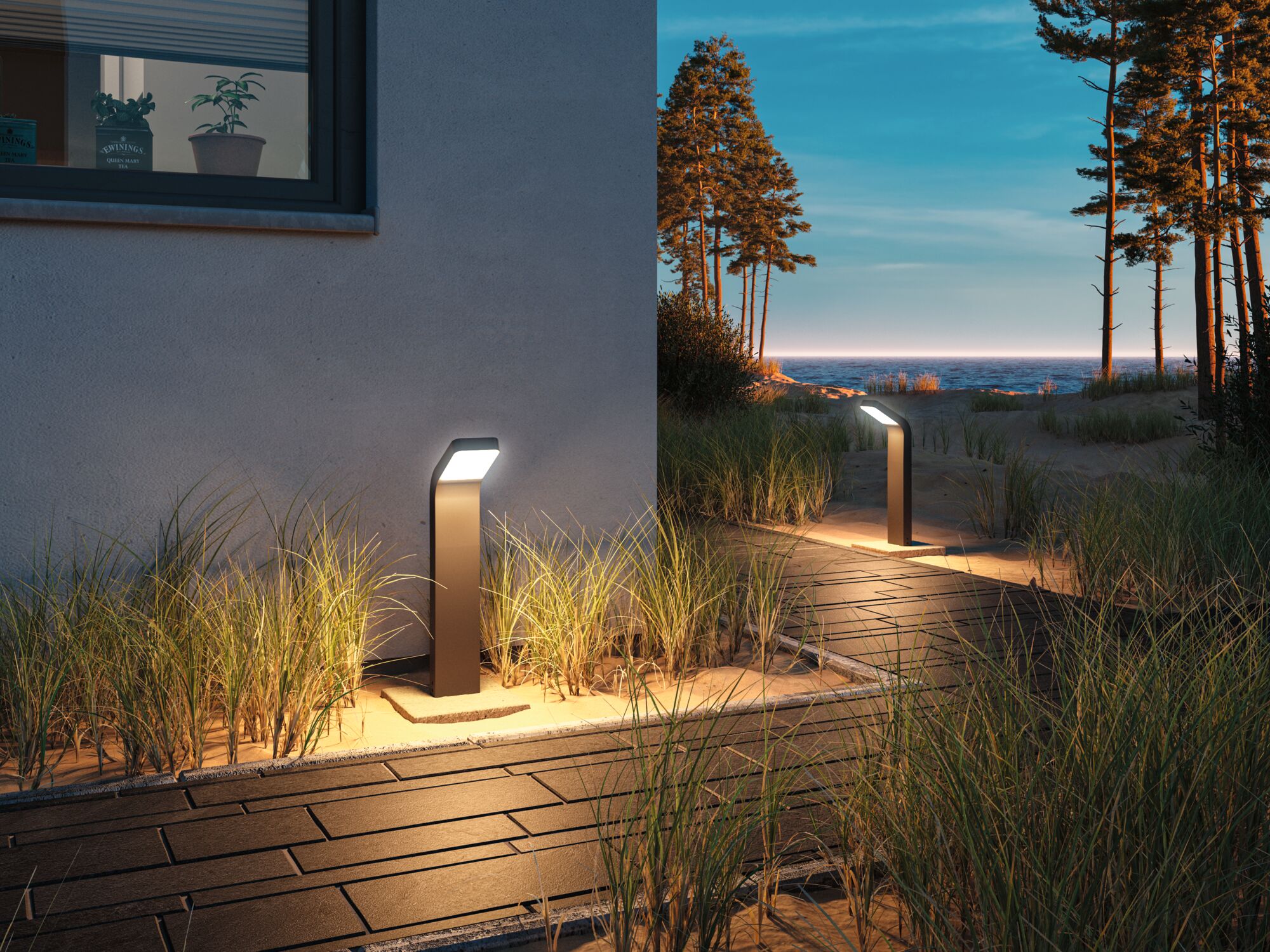 Modern anthracite metal outdoor lights illuminate sandy path with grass at dusk by the sea