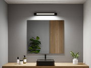 Black ceramic sink on wooden countertop with mirror and modern LED wall light in bathroom.