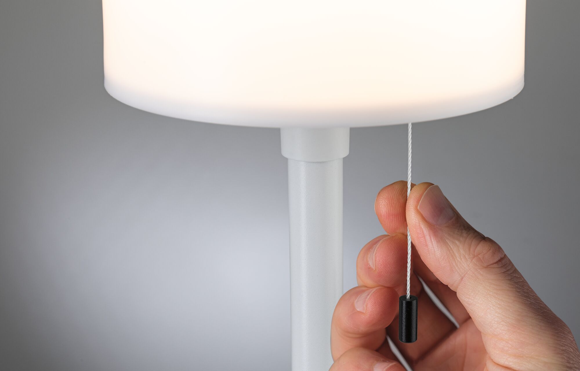 Hand zieht weißen Zugschalter an moderner weißer Tischlampe mit rundem Lampenschirm aus Kunststoff