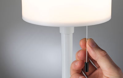 Hand zieht weißen Zugschalter an moderner weißer Tischlampe mit rundem Lampenschirm aus Kunststoff