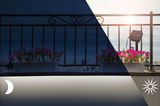 Modern black outdoor spotlight illuminating pink flowers on balcony during day and night