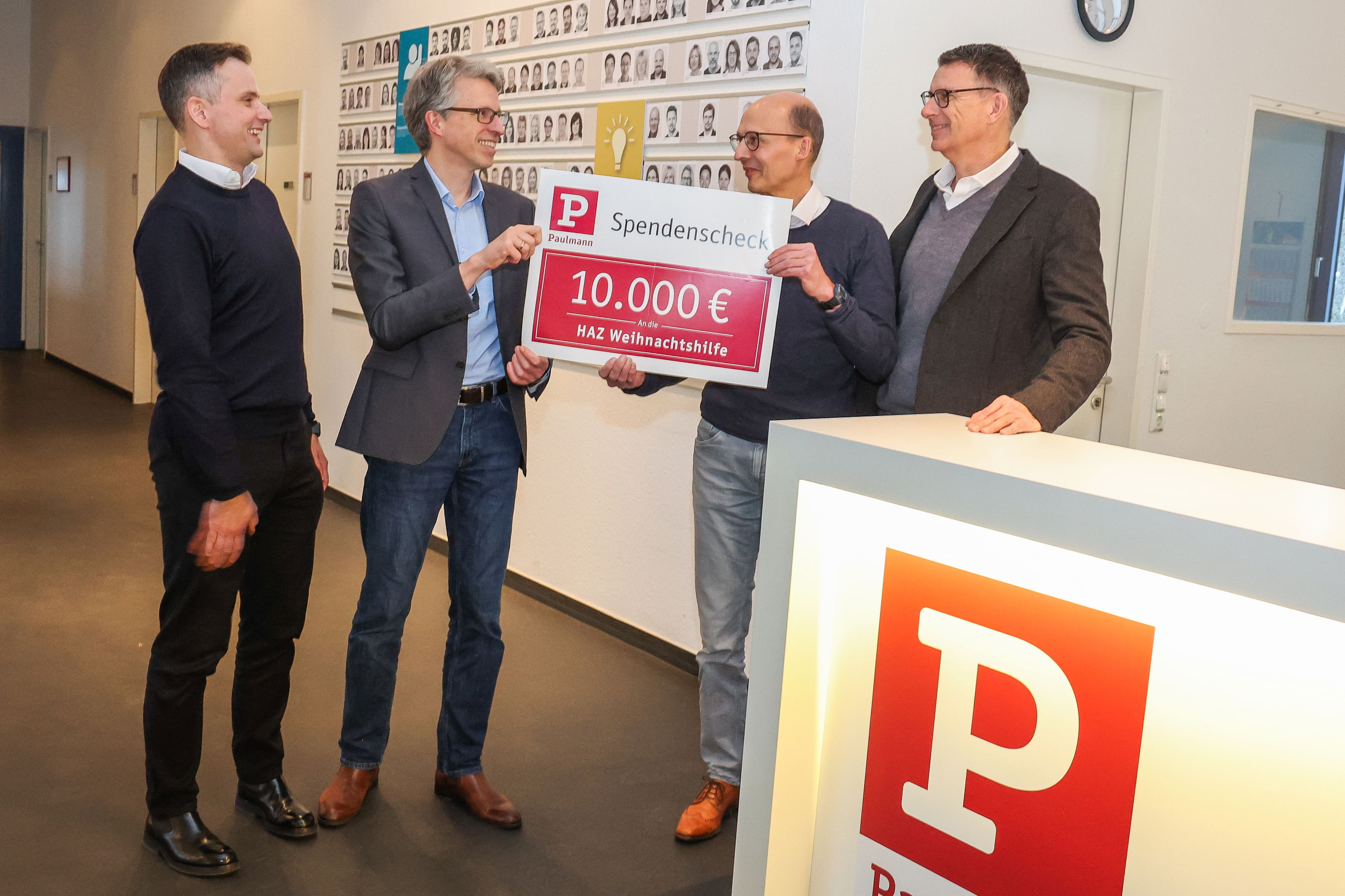 Vier mannen overhandigen symbolische donatiecheque van 10.000 euro aan HAZ kersthulp op kantoor.