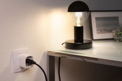 Zwarte tafellamp met halve bol lamp op glazen blad naast witte stopcontact met zwarte kabel