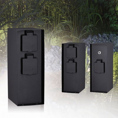 Three black metal outdoor power sockets with protective covers in a garden setting