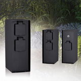 Three black metal outdoor power sockets with protective covers in a garden setting