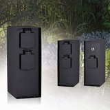 Three black metal outdoor power sockets with protective covers in a garden setting