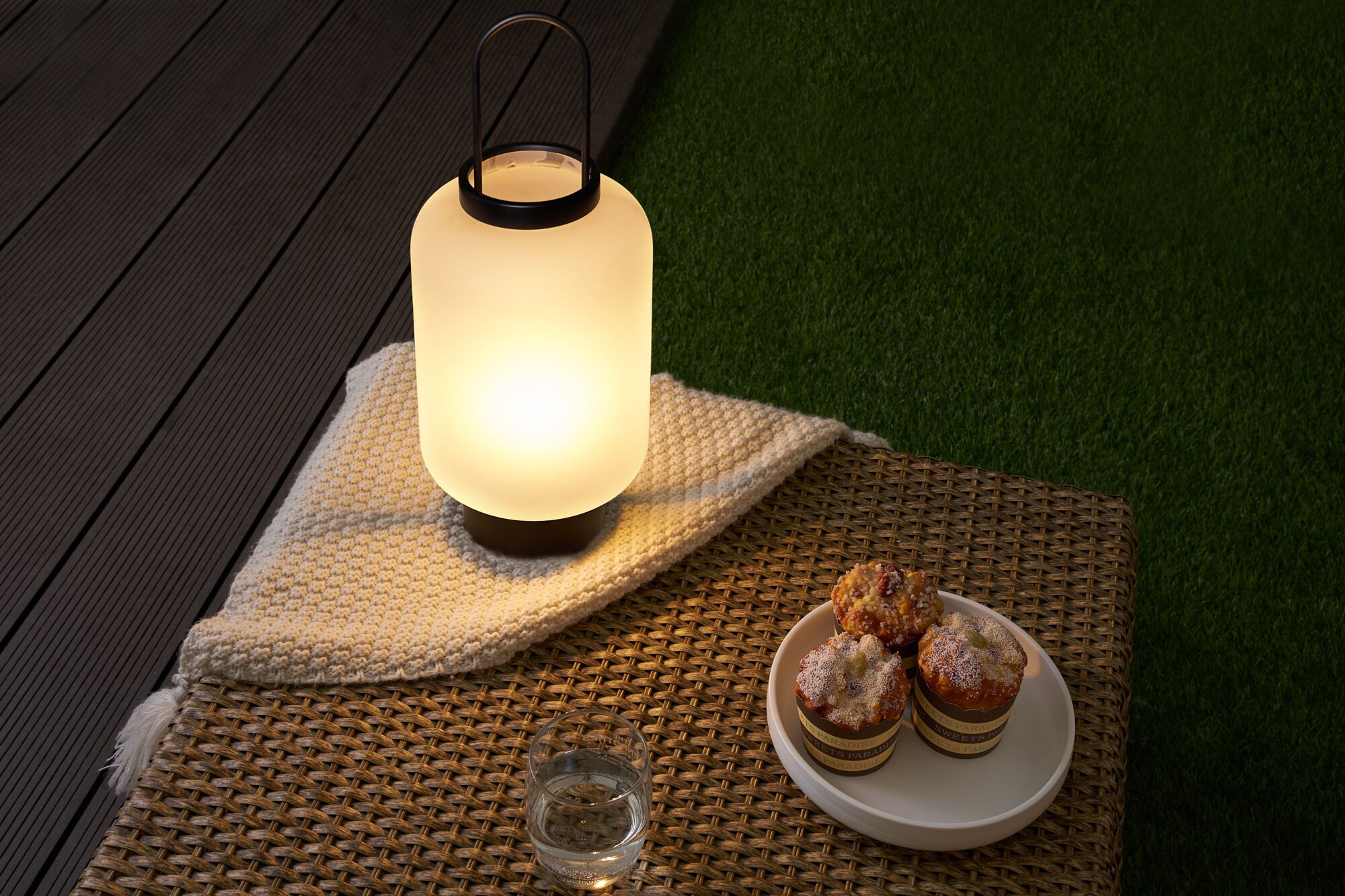 Lampe de table extérieure moderne en verre blanc mat avec poignée noire sur table en osier avec muffins.