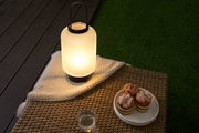 Modern outdoor table lamp with frosted glass and black handle on rattan furniture with muffins.