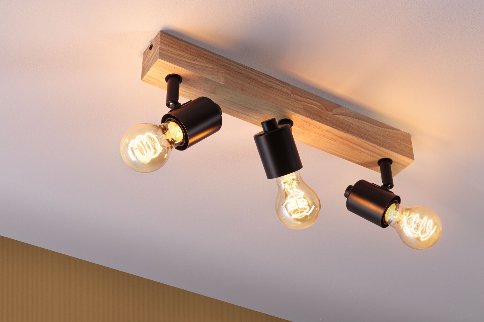 Deckenleuchte mit Holzträger und drei schwarzen Metalllampen mit warmweißen LED-Glühbirnen für Wohnräume