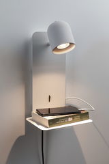 Modern white metal wall spotlight with shelf, illuminating book and smartphone for charging.