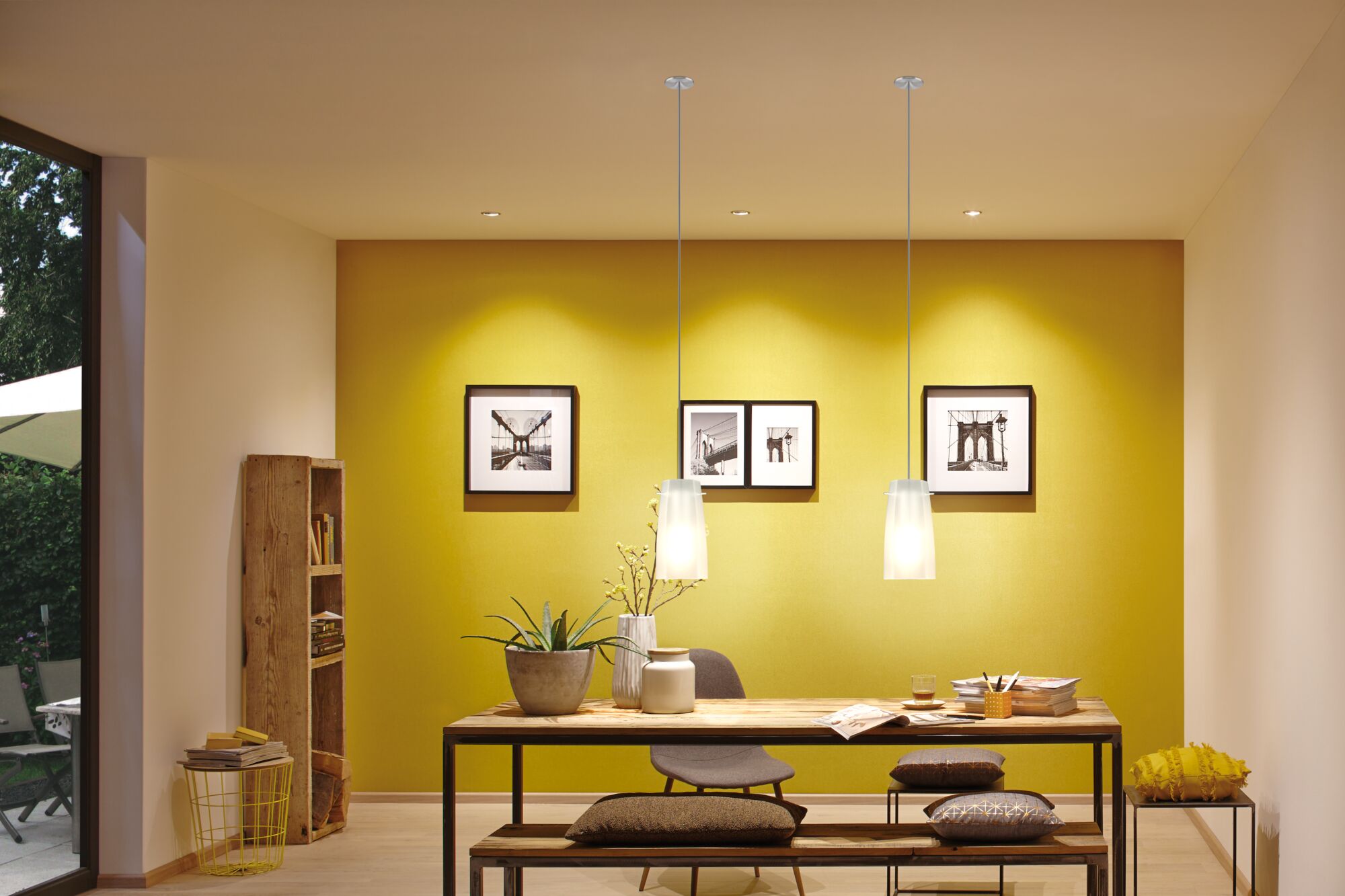 Modern dining area with wooden table, grey chair, yellow wall, and two white glass pendant lights.