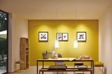 Modern dining area with wooden table, grey chair, yellow wall, and two white glass pendant lights.