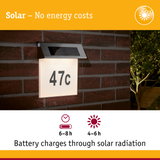 Solar-powered house number light with stainless steel top and white illuminated panel on red brick wall
