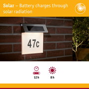 Solar-powered house number light with stainless steel top and white illuminated panel on red brick wall