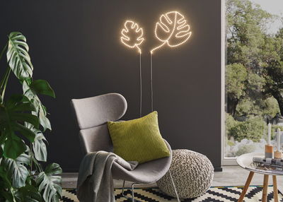 Bladvormige LED-wandlamp met warm wit licht aan donkere muur in moderne woonkamer.