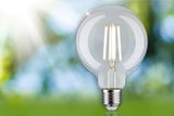 Clear LED filament bulb with E27 base against a green and blue blurred background