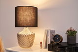 Table lamp with brown fabric shade and textured clear glass base on white table with clock and plant