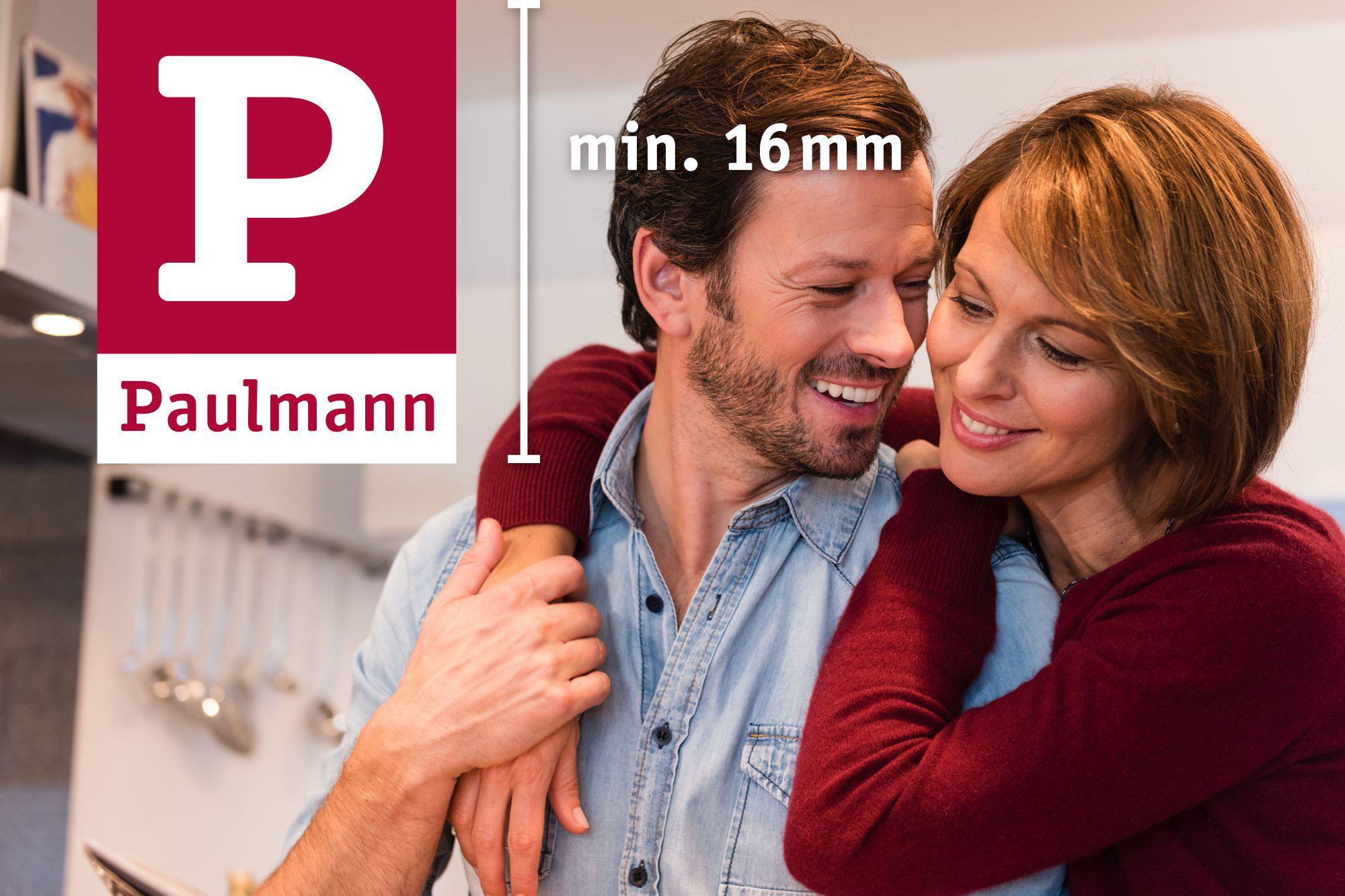 Glückliches Paar umarmt sich in moderner Küche mit Paulmann Logo und Mindestmaß 16 mm.