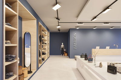 Moderner Modegeschäft-Innenraum mit blauen Wänden, Holzregalen, Spiegel und Beleuchtungssystem.