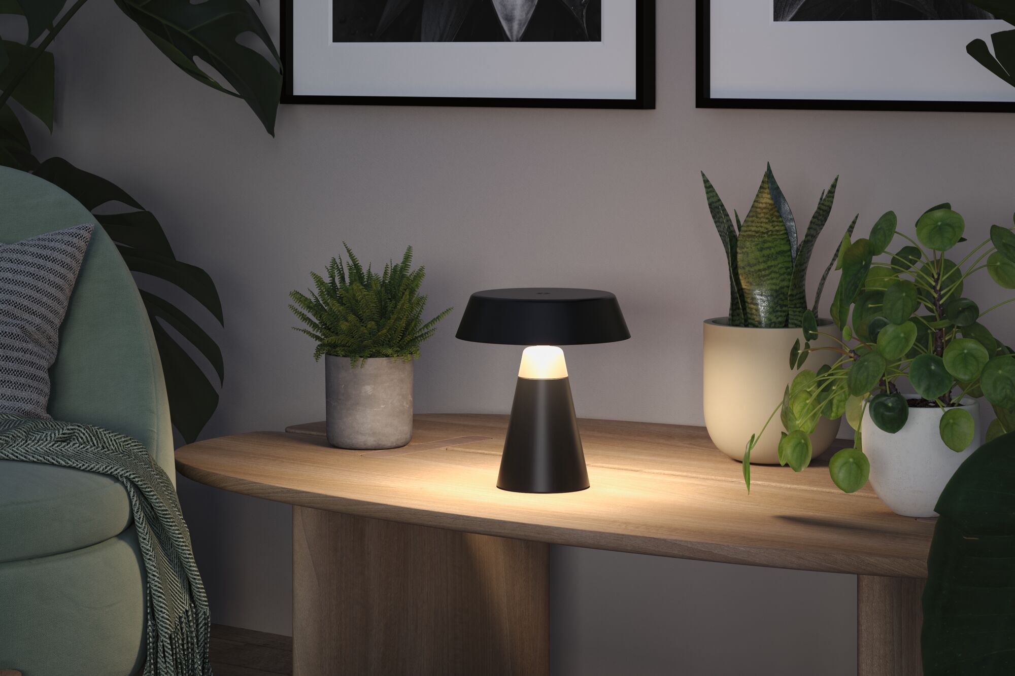 Schwarze Tischlampe aus Metall mit warmweißem Licht auf Holztisch neben grünen Zimmerpflanzen