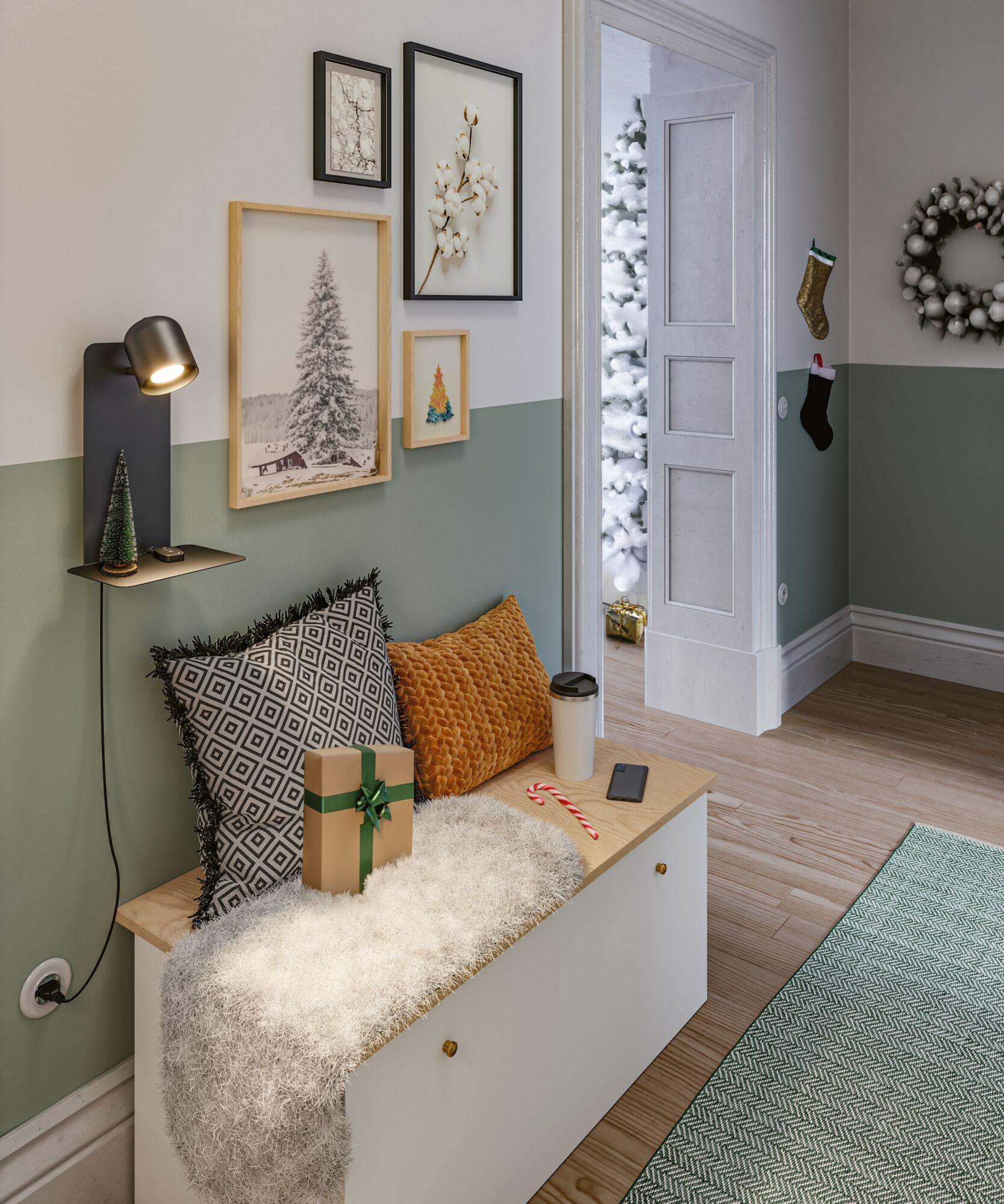 Coin salon confortable avec coussins, cadeau et lampe murale dans une pièce verte et blanche décorée pour Noël avec branche de pin.