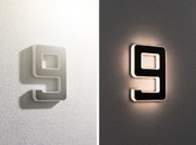 Modern LED wall light shaped as number 9, white and black, emitting warm light for home decor