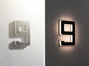 Modern LED wall light shaped as number 9, white and black, emitting warm light for home decor