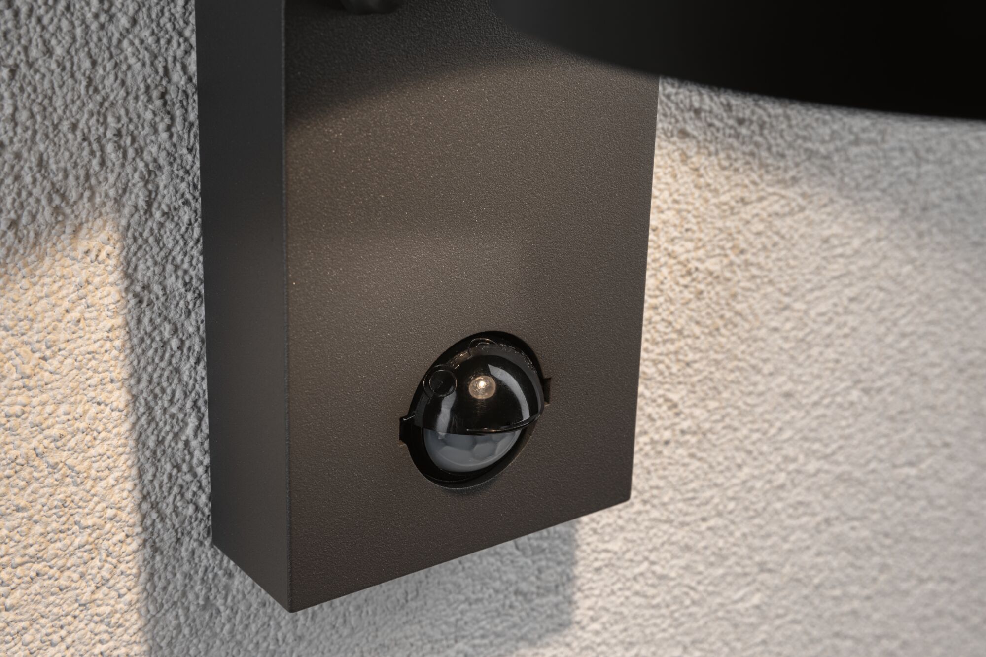 Zwarte bewegingssensor op gestructureerde witte muur voor buitenverlichting en beveiliging.