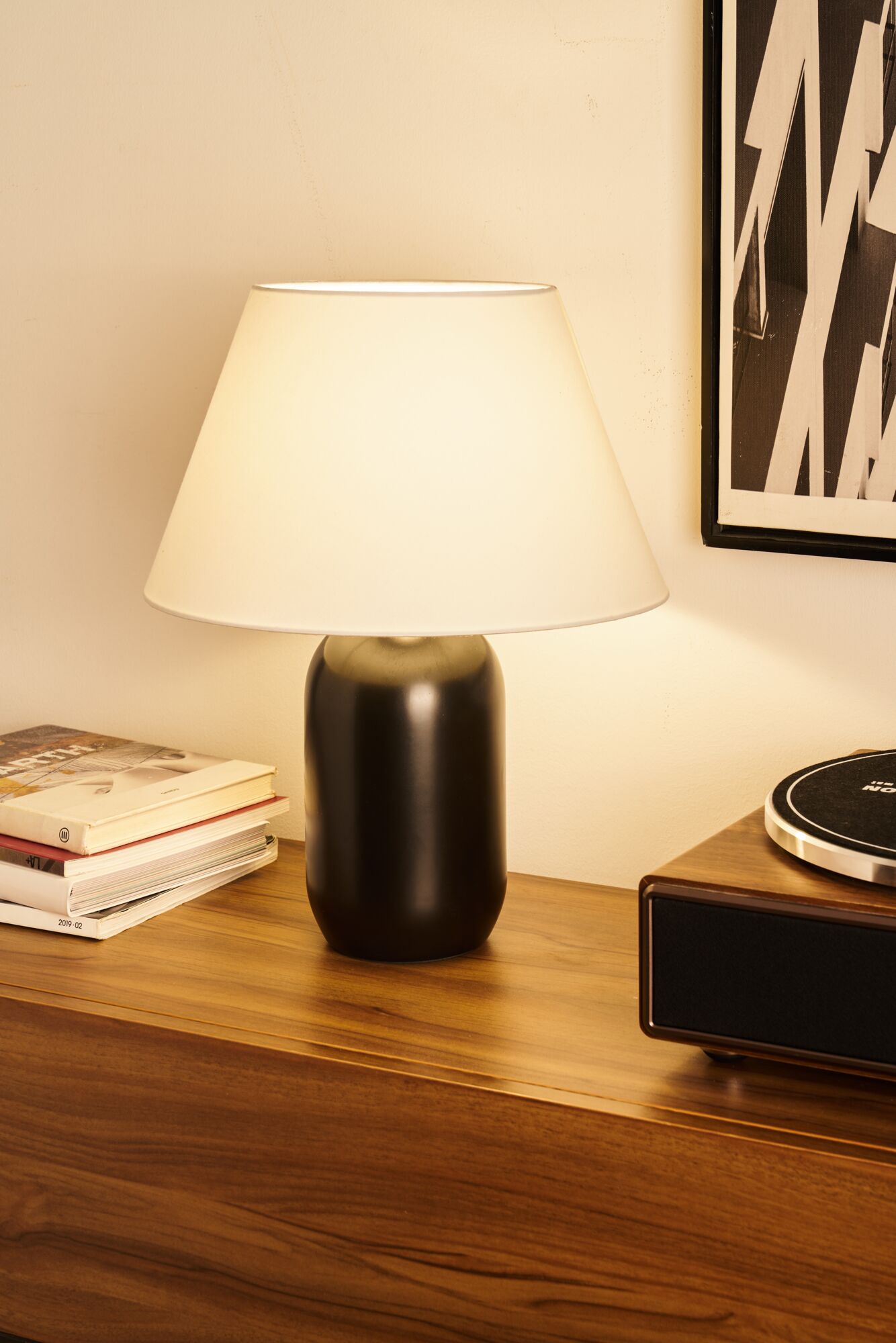 Moderne Tischlampe mit schwarzem Keramikfuß und weißem Stoffschirm auf Holzkommode im Wohnzimmer