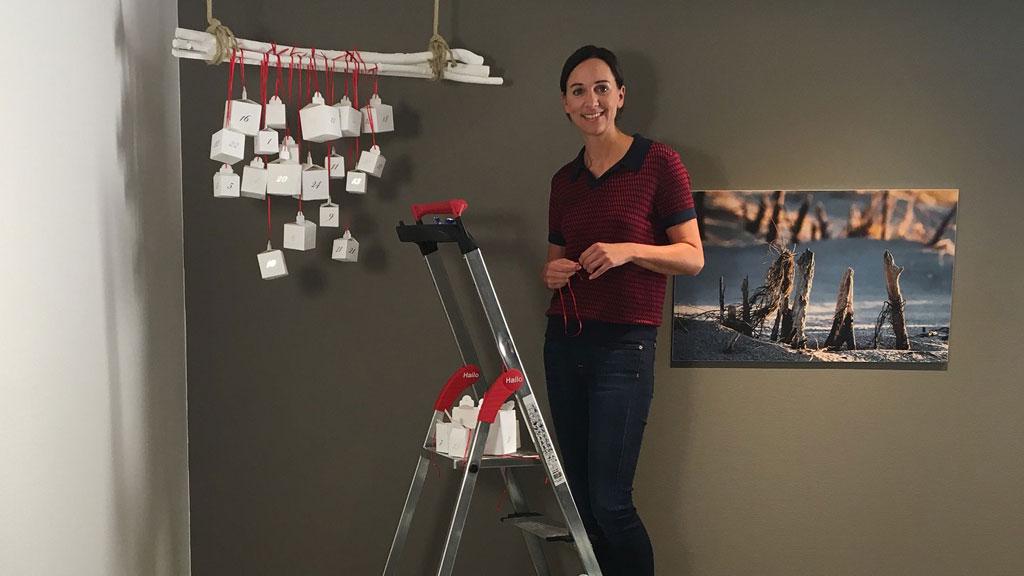 Femme décorant un calendrier de l'Avent blanc avec rubans rouges sur mur marron, échelle en aluminium