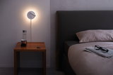 Applique murale blanche en métal avec lumière chaude au-dessus de la table de chevet en bois près du lit sombre