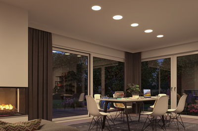 Wohnzimmer mit moderner Decken-Einbauleuchte in warmweiß, großflächige Fenster und Kamin für gemütliche Beleuchtung