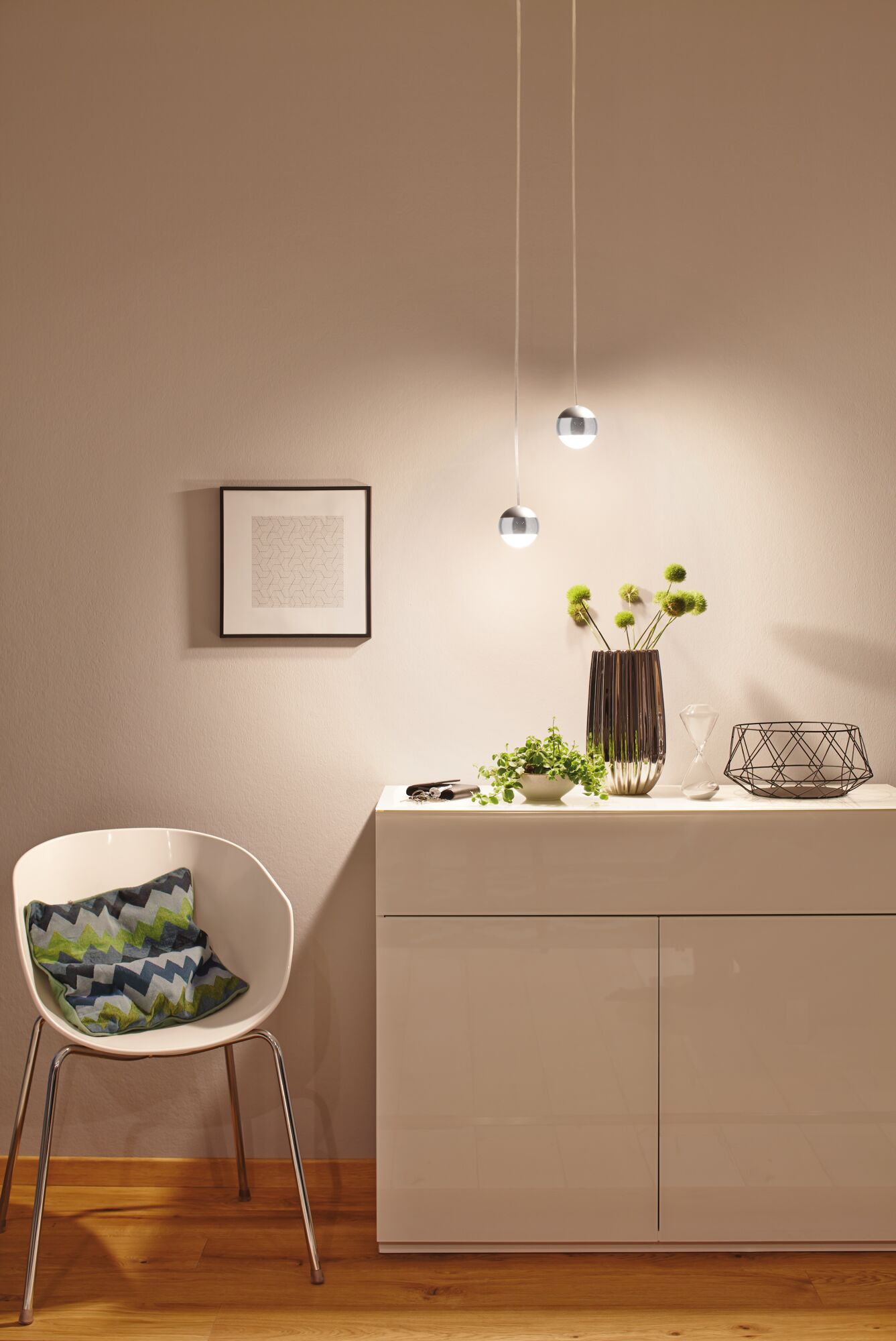 Moderne Pendelleuchten mit Kugelform in Chrom und Weiß beleuchten minimalistische Wohnzimmereinrichtung mit Pflanzen.