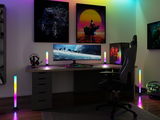 Modern gaming setup with RGB LED light bars, large monitor, and ergonomic chair in a dark room.