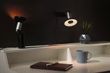Modern black and silver LED desk spotlight with warm light on white desk with mug and plant