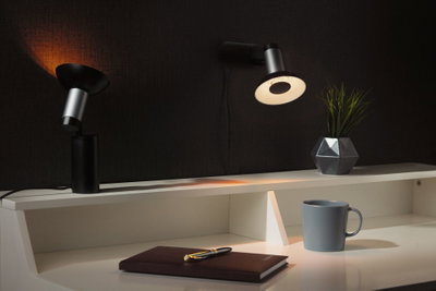 Spot LED de bureau moderne noir et argent avec lumière chaude sur bureau blanc avec tasse et plante