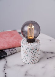 Round smoked glass bulb on white terrazzo base with colorful chips, decorative table lamp for interior lighting