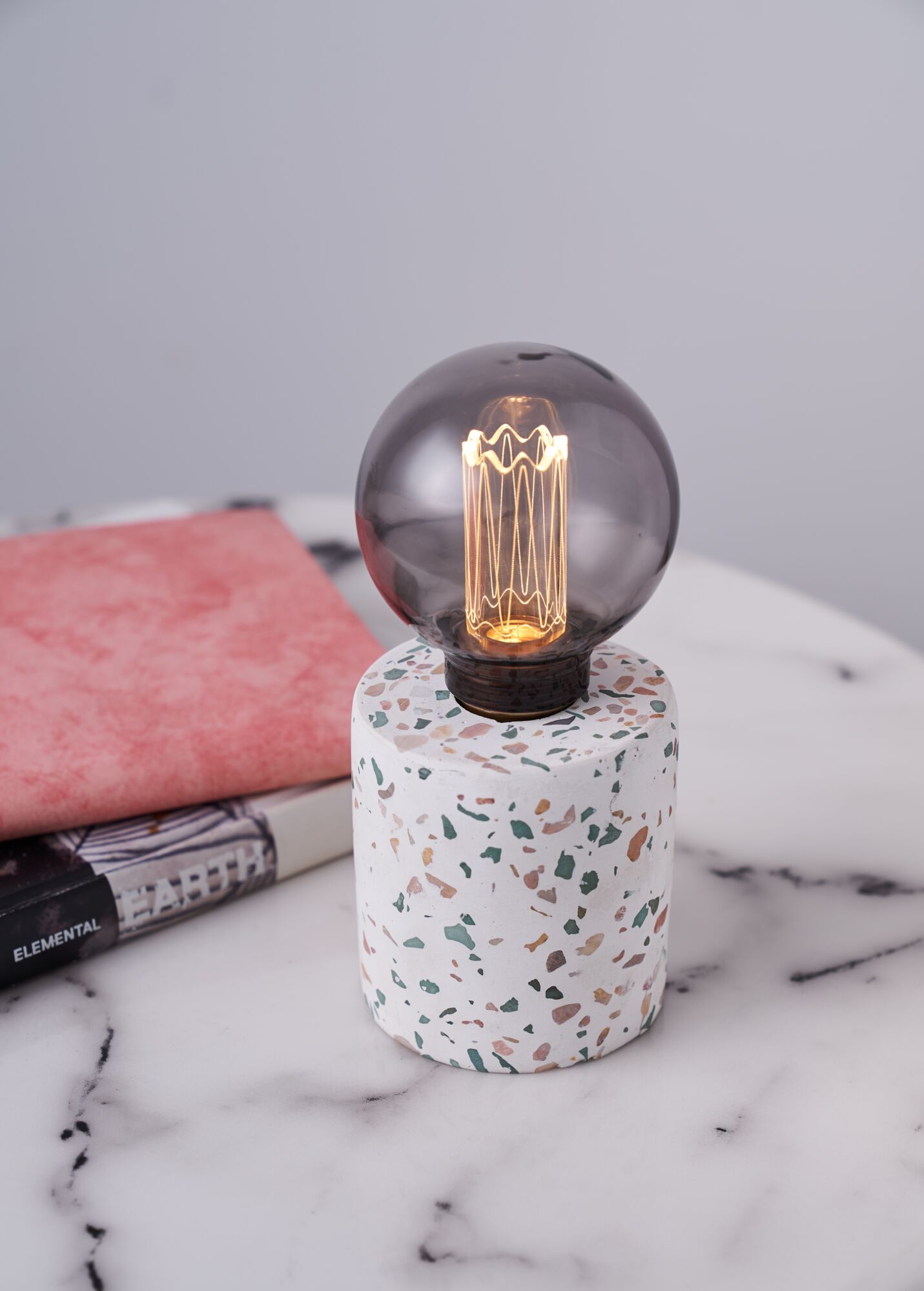 Round smoked glass bulb on white terrazzo base with colorful chips, decorative table lamp for interior lighting