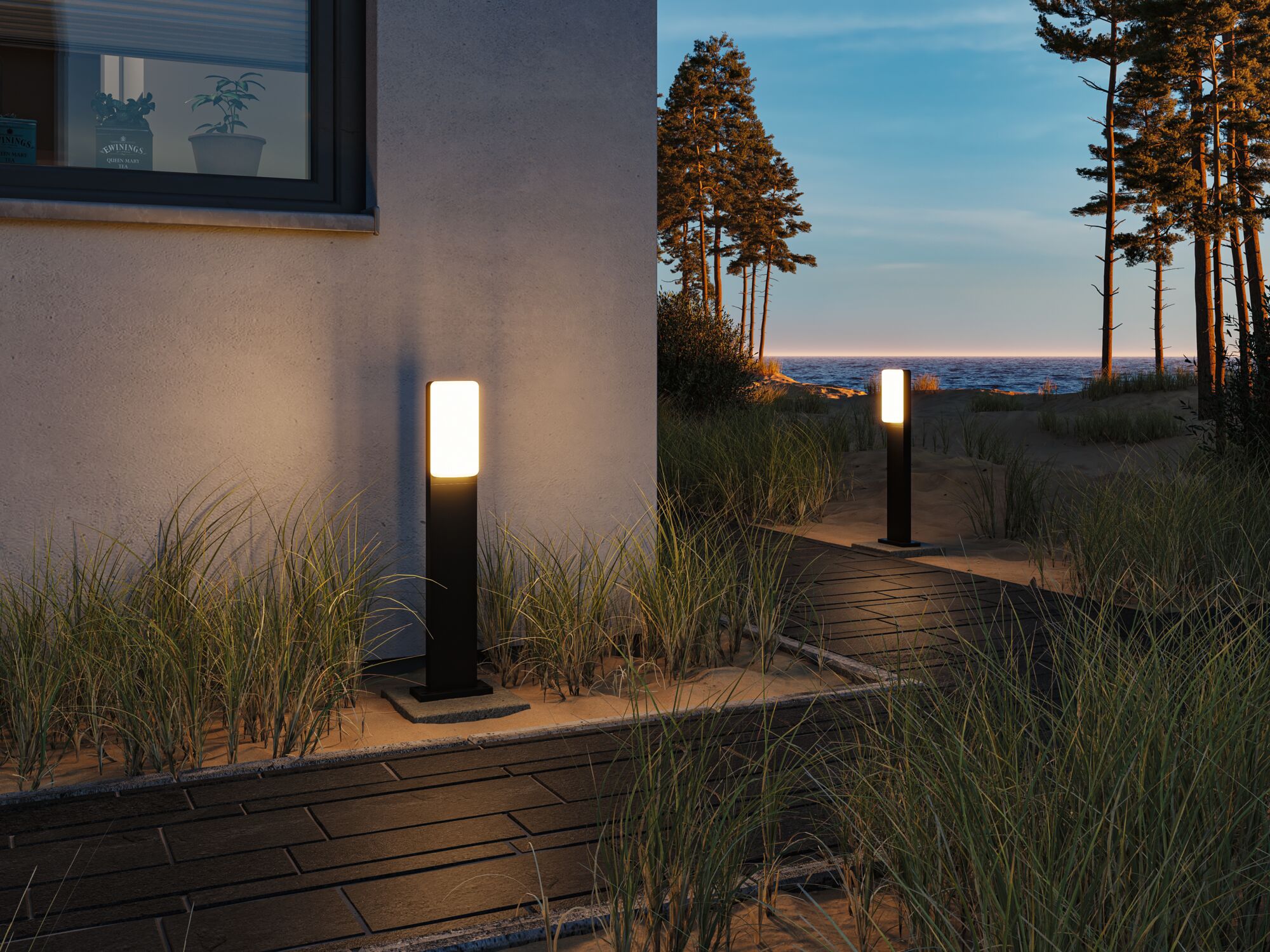 Modern black outdoor lamp with white light on path by house and dune landscape at sunset