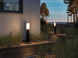 Modern black outdoor lamp with white light on path by house and dune landscape at sunset
