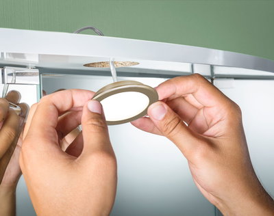 Hand installing round gold-colored LED recessed spotlight under white furniture for indoor lighting