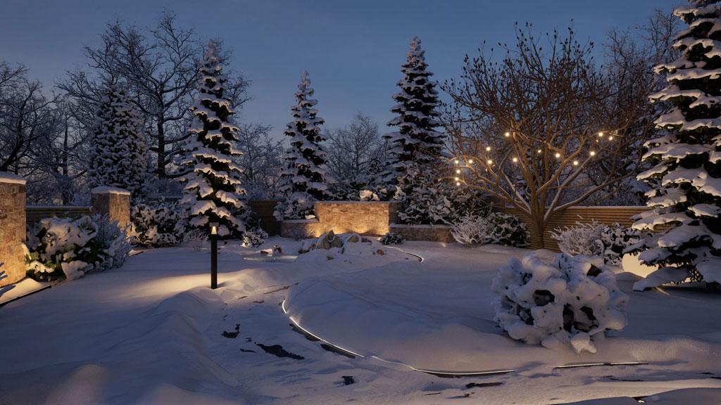 Vinterhavebelysning med varm hvide LED-lys på træer og stier i et snedækket udendørsområde.